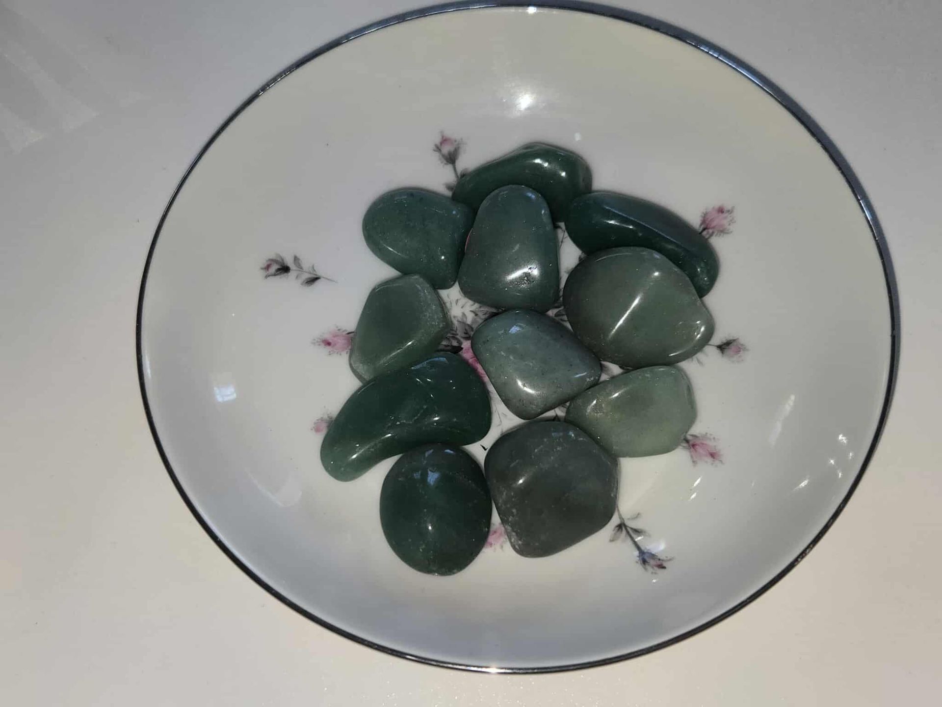 Green tumbled stones in a white bowl with floral details.