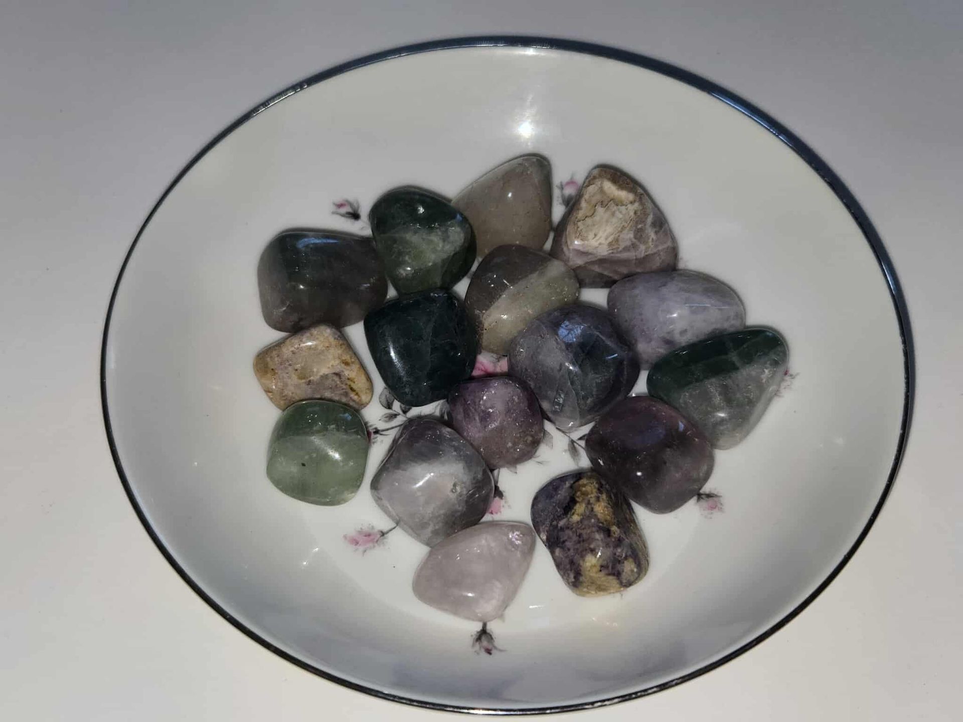 A white bowl holding an assortment of polished, colorful gemstones.