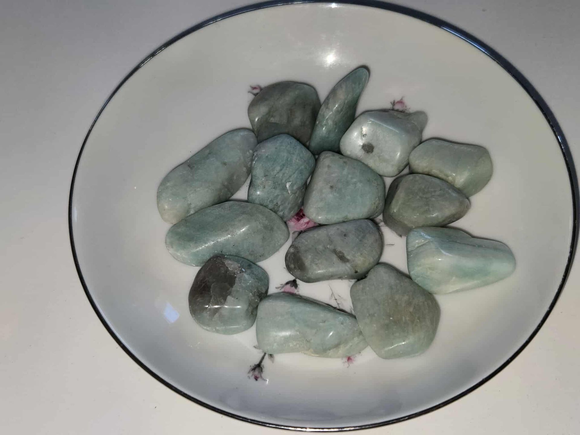 Rounded, teal-green tumbled stones in a white bowl with a dark blue rim.