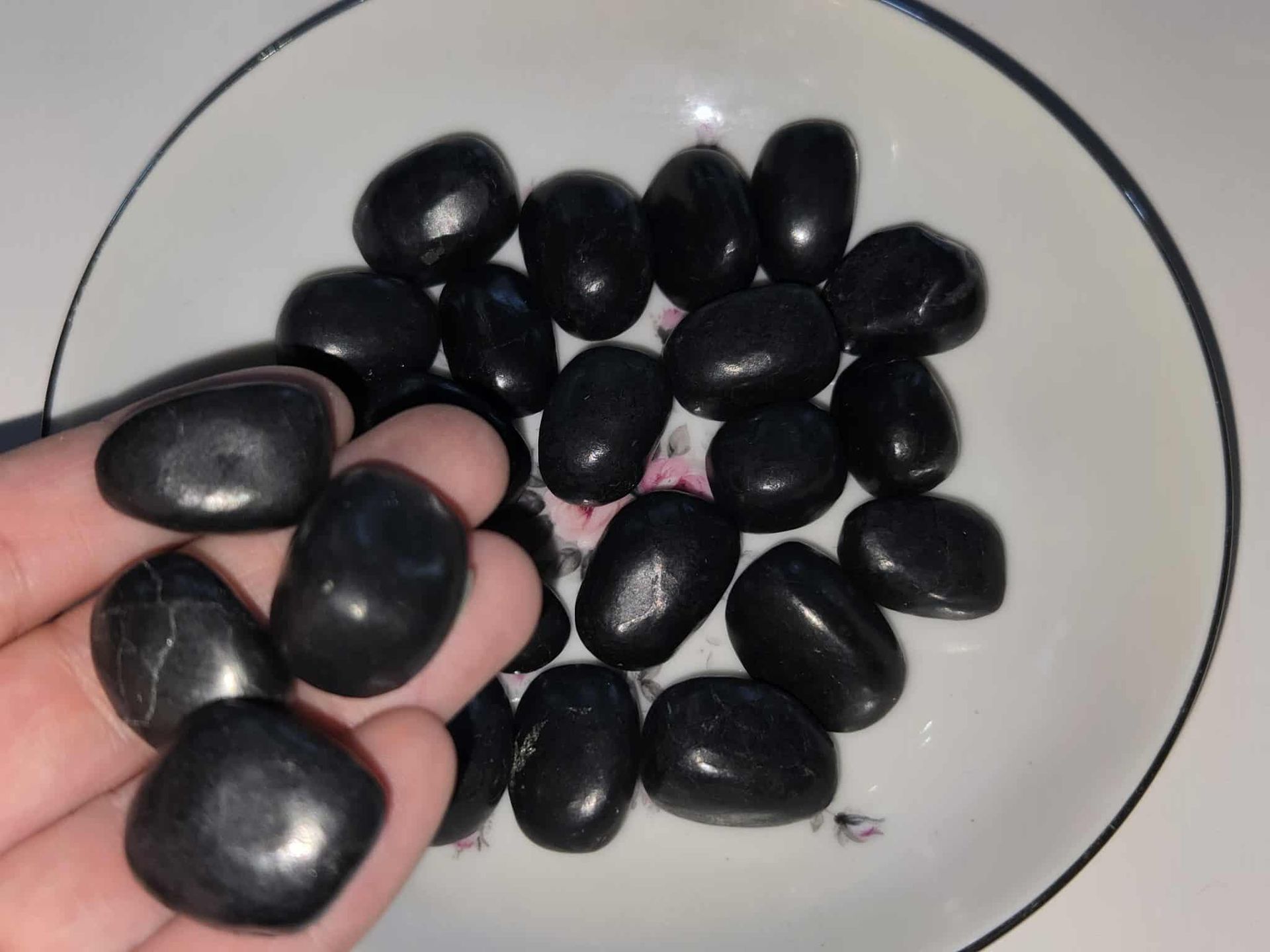 Black candies in a white and floral-patterned dish on a white surface.
