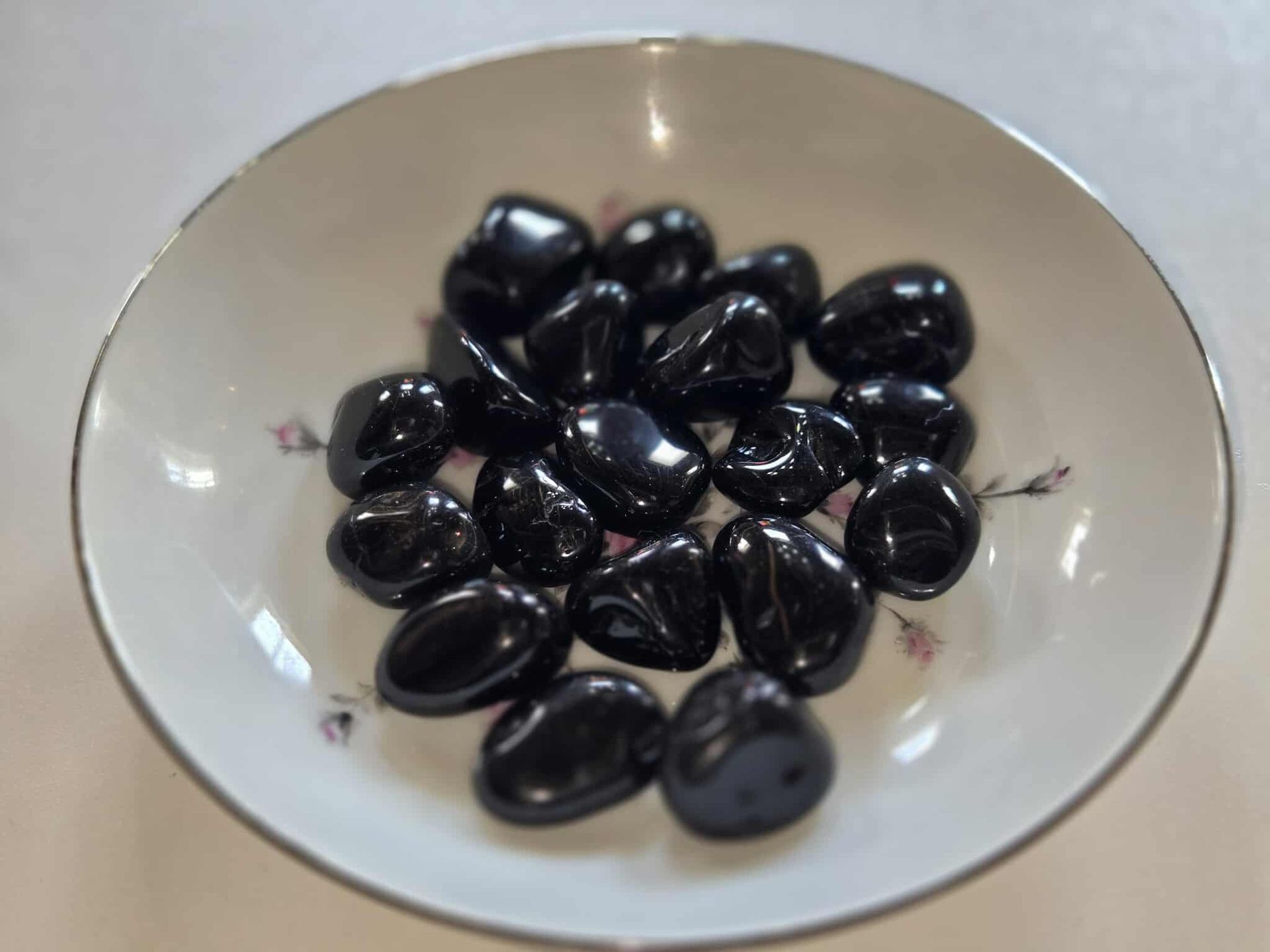 Black polished stones in a white bowl with floral designs.