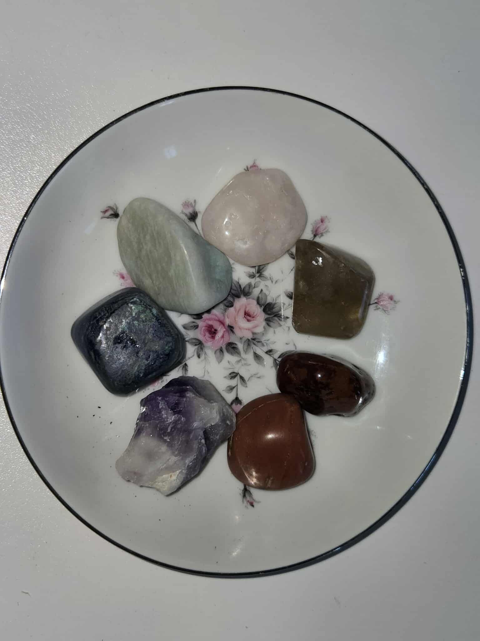 Seven polished gemstones arranged on a floral-patterned white plate.