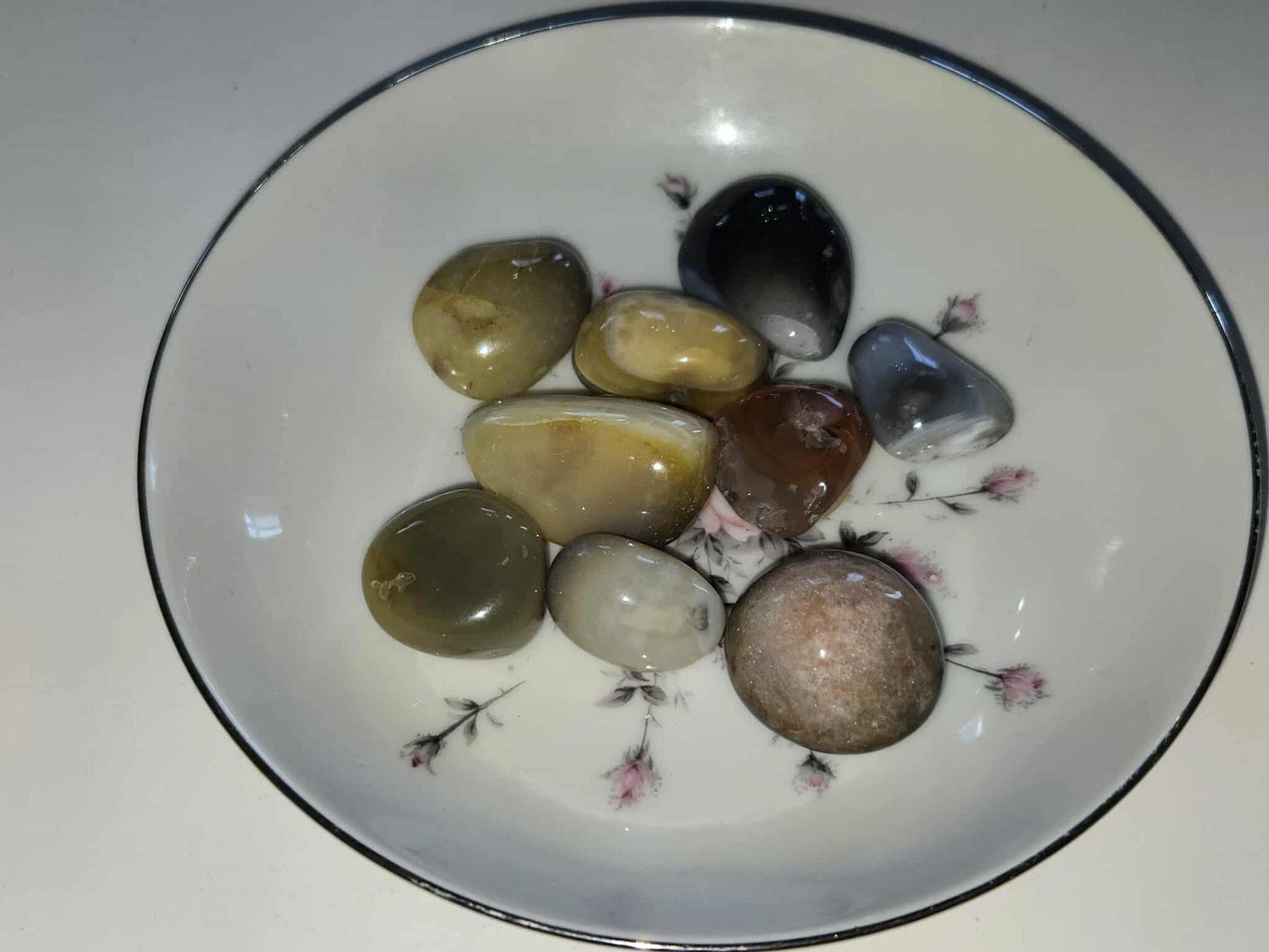 Smooth, colorful stones in a decorative floral bowl on a white surface.