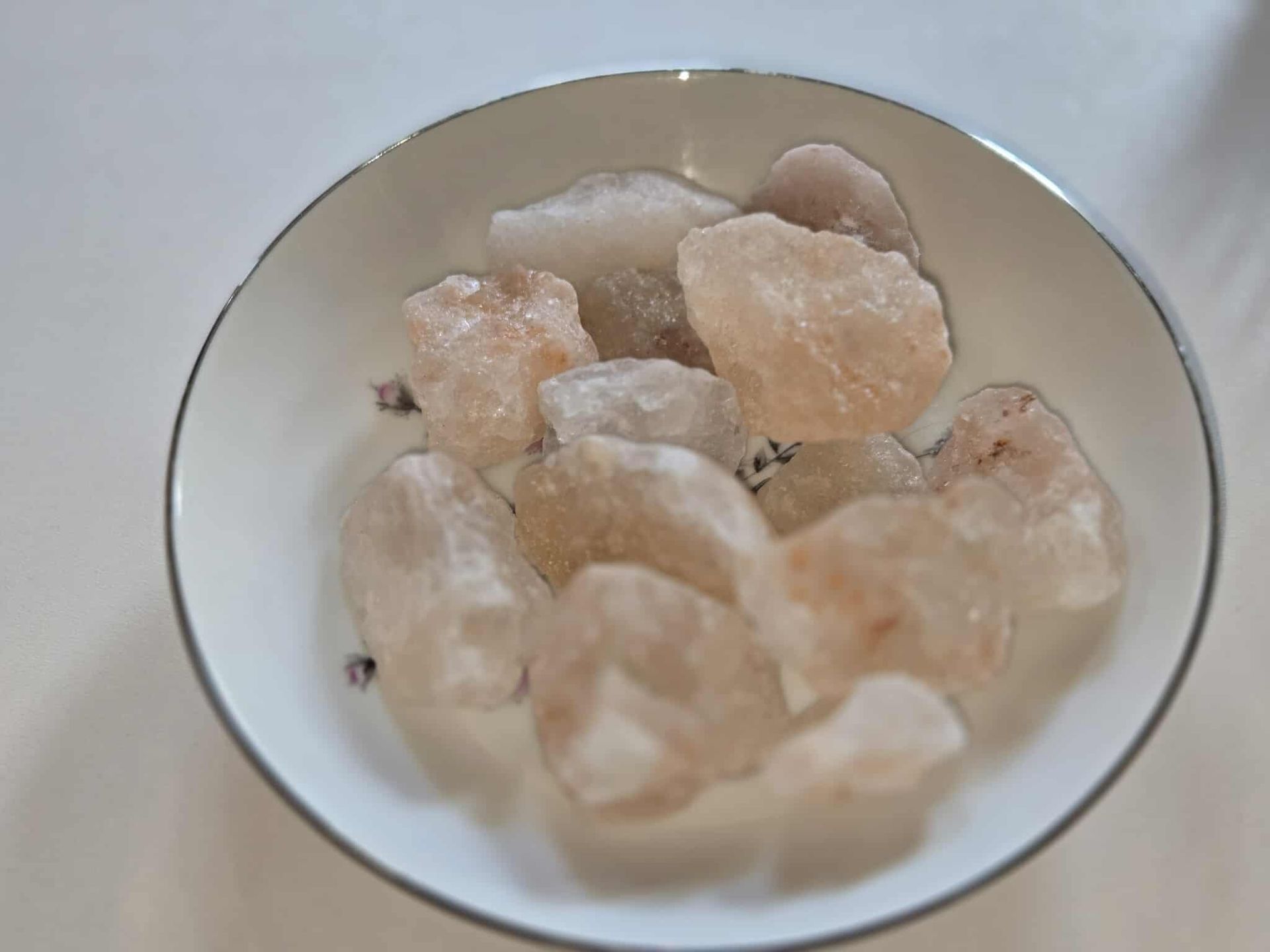 Pink Himalayan salt chunks in a white bowl with a silver rim.