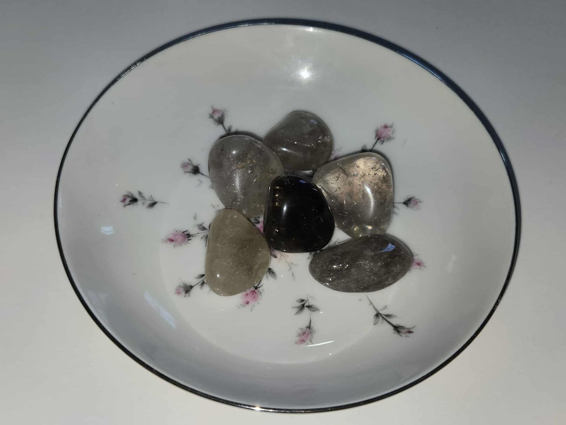 Small white bowl with floral design, holding several gray and black polished stones.