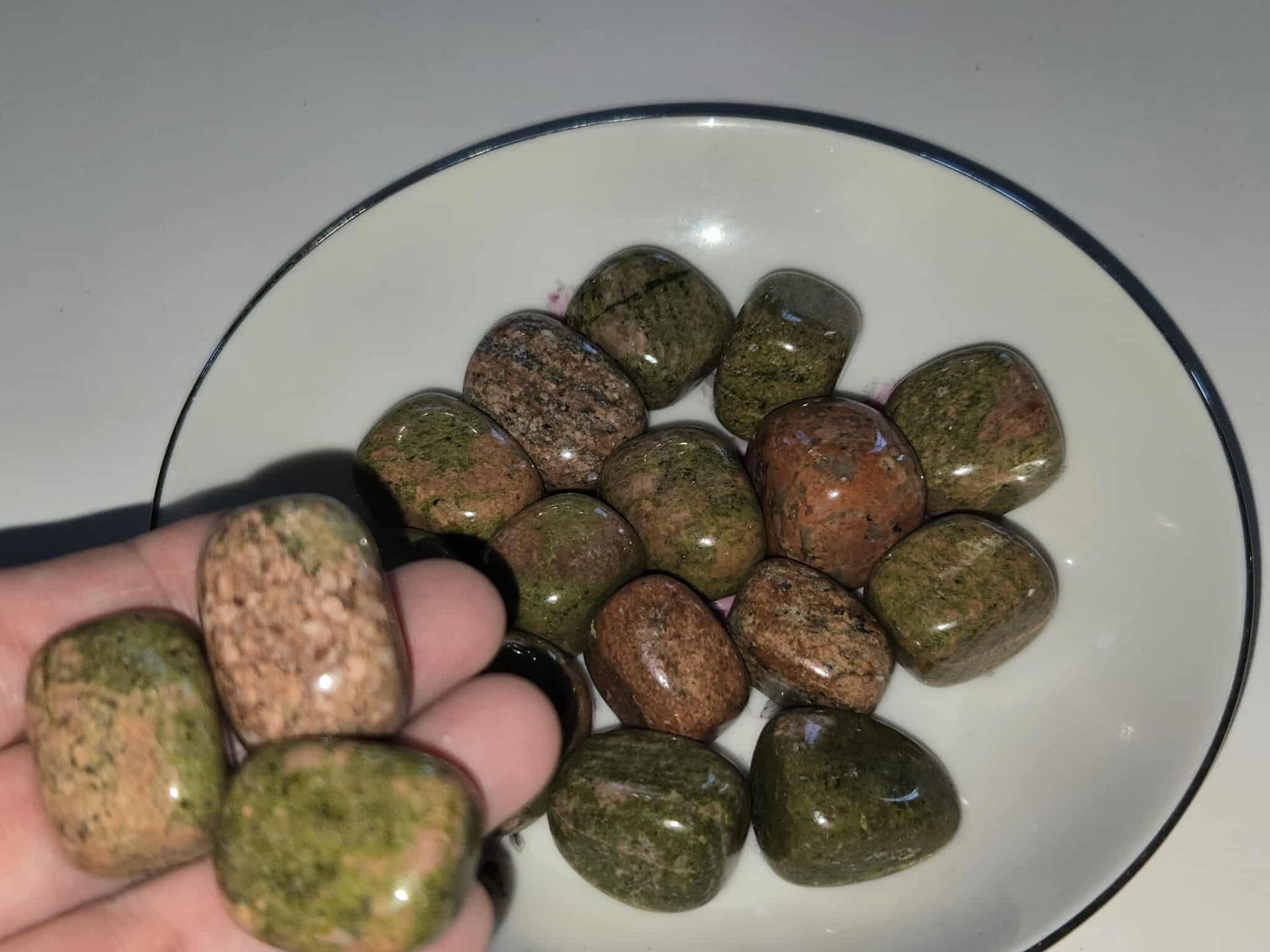 Tumbled unakite stones, green and pink hues, arranged in a white bowl with a blue rim.
