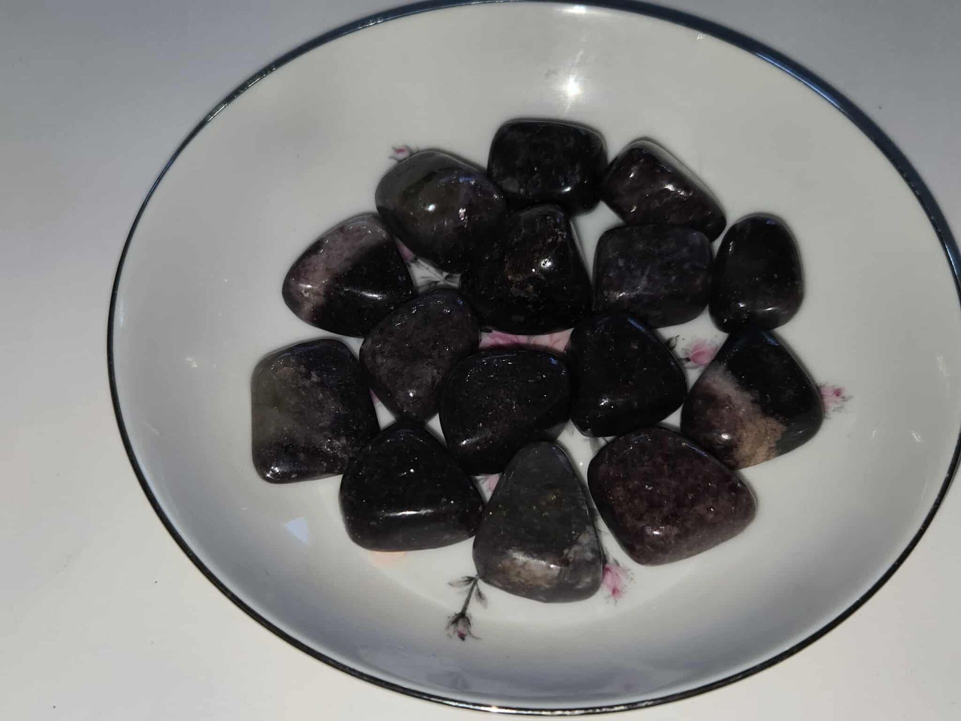 Black and purple polished stones in a white bowl with a floral design.