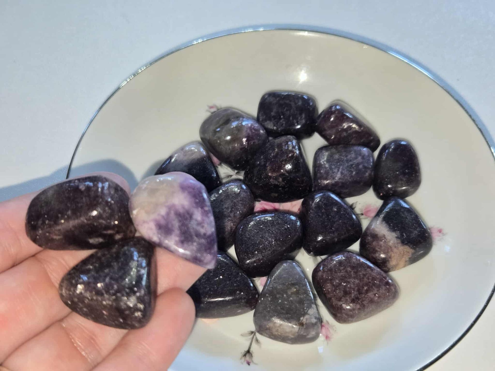 Black and purple polished stones in a white bowl with a floral design.