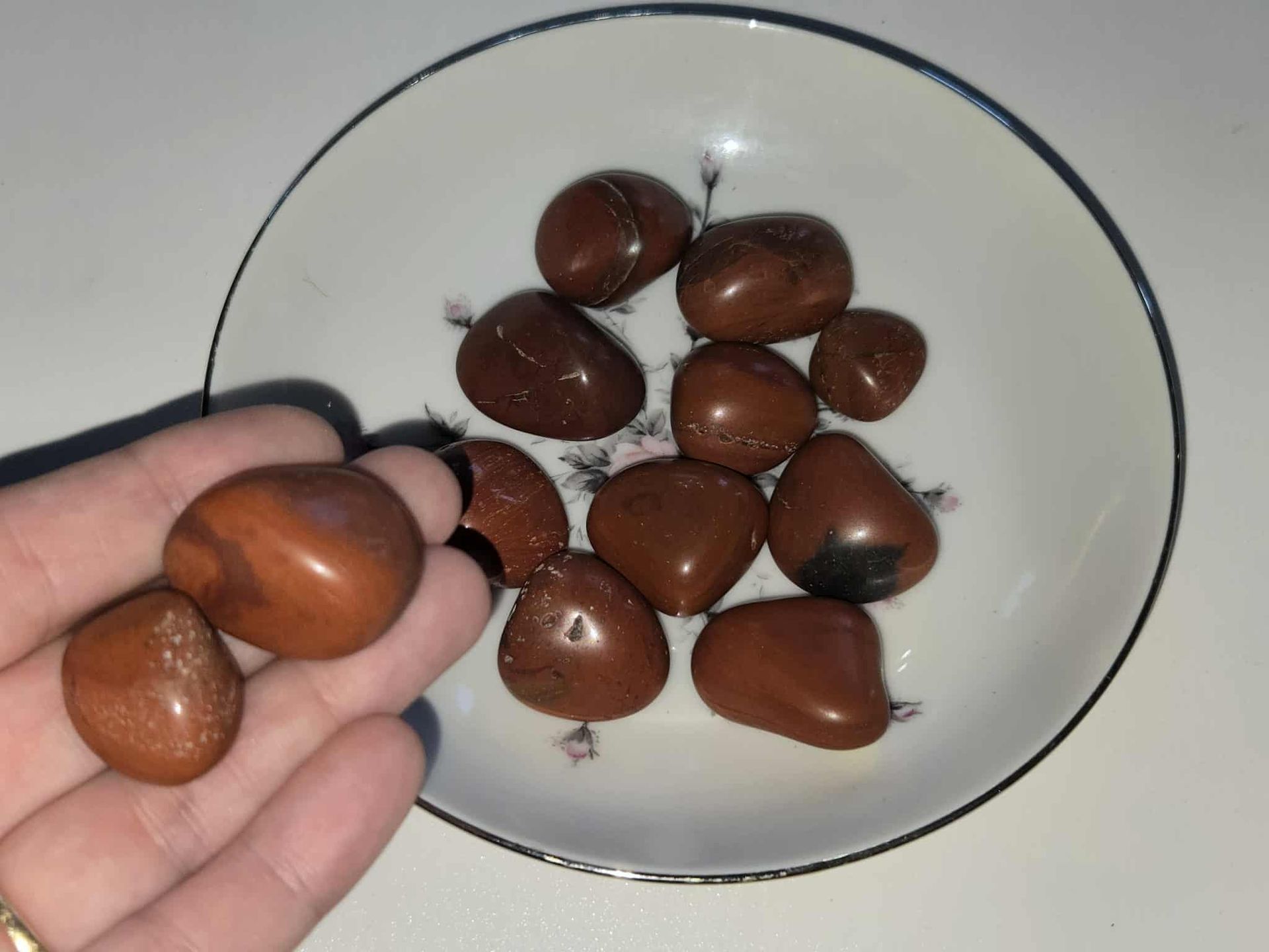 Brown polished stones in a floral decorated white bowl with a blue rim on a white surface.