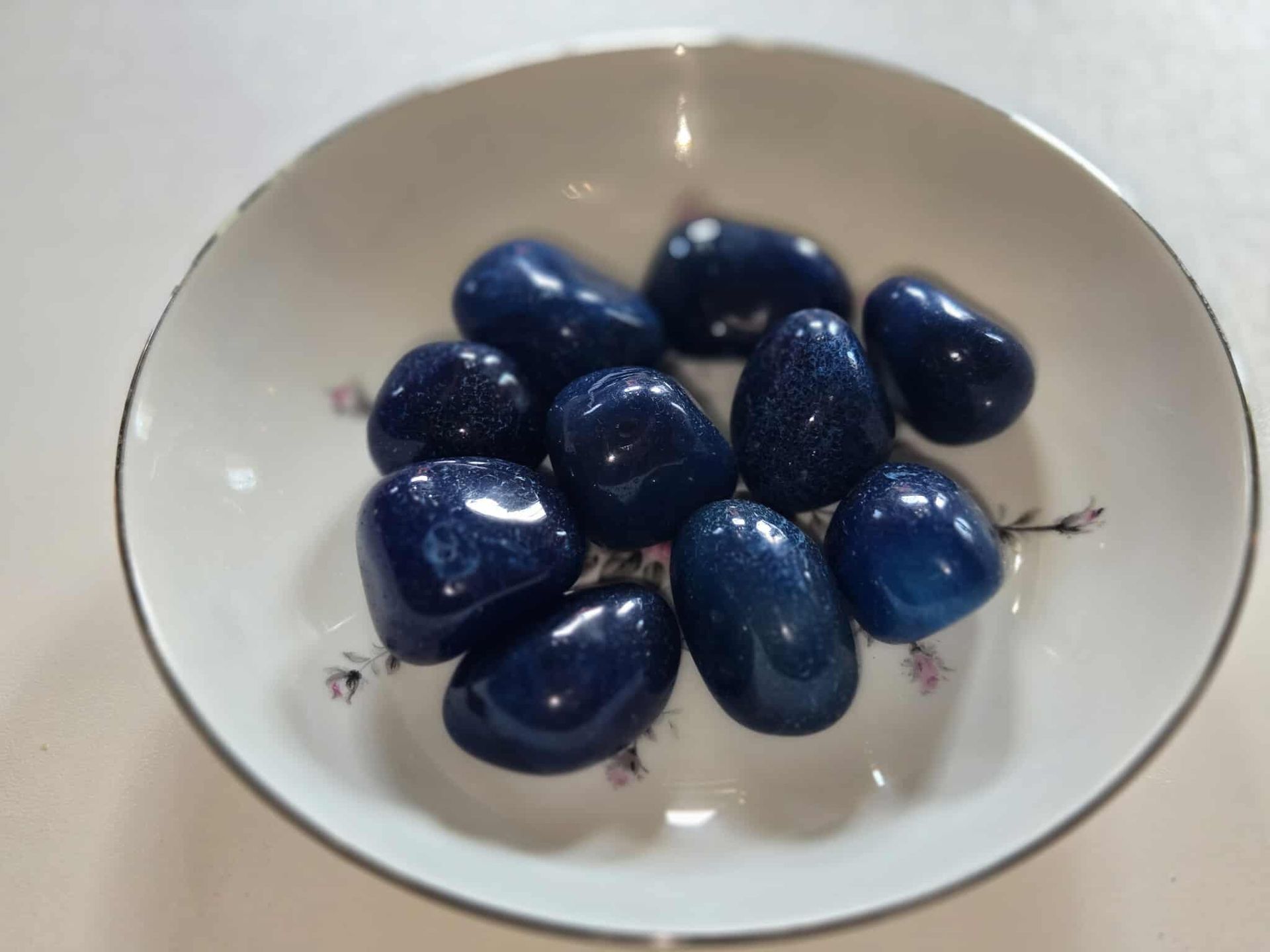Blue goldstone tumbled stones in a white decorative dish.