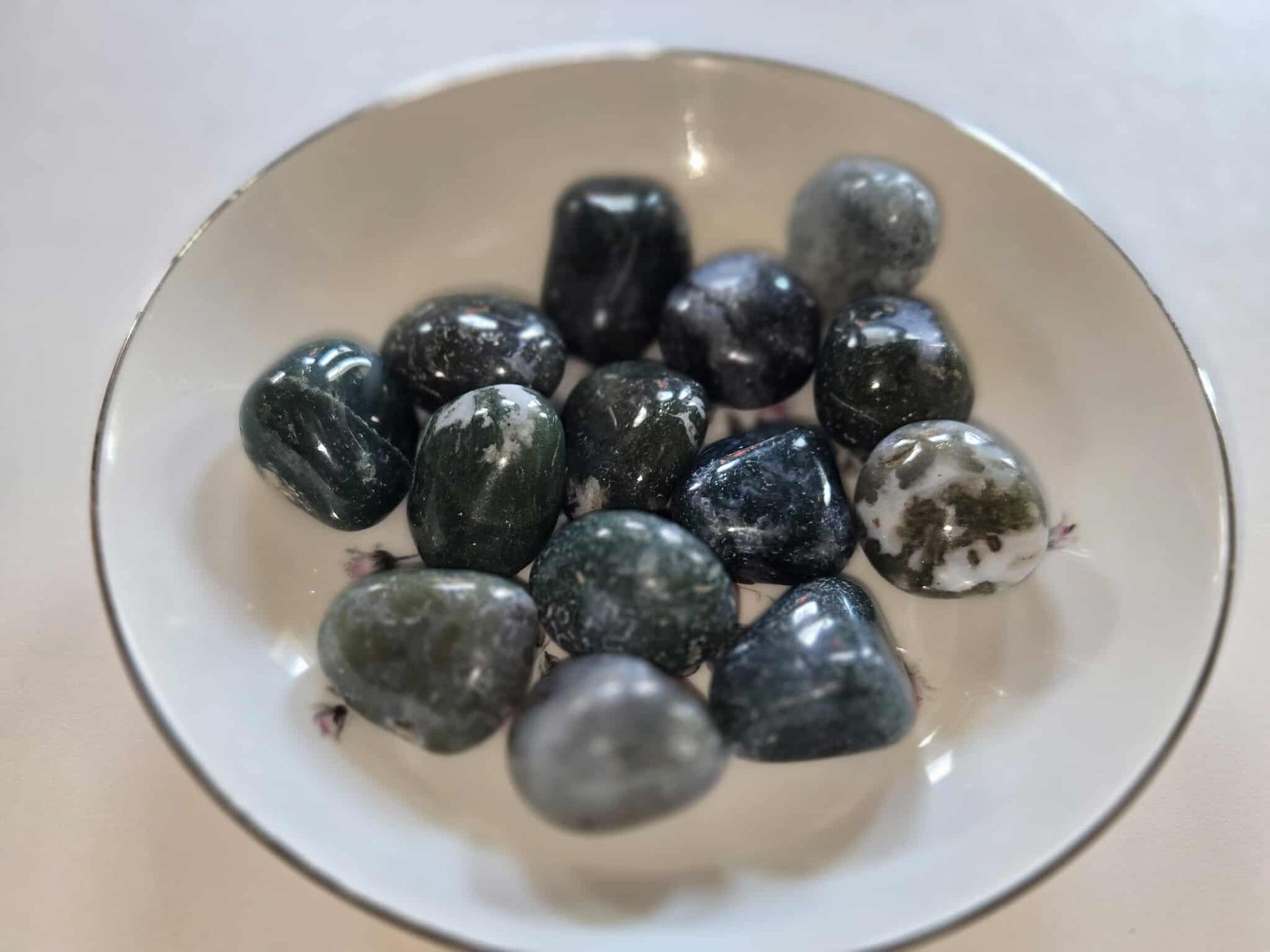 A white bowl filled with a collection of smooth, dark green and grey tumbled stones.