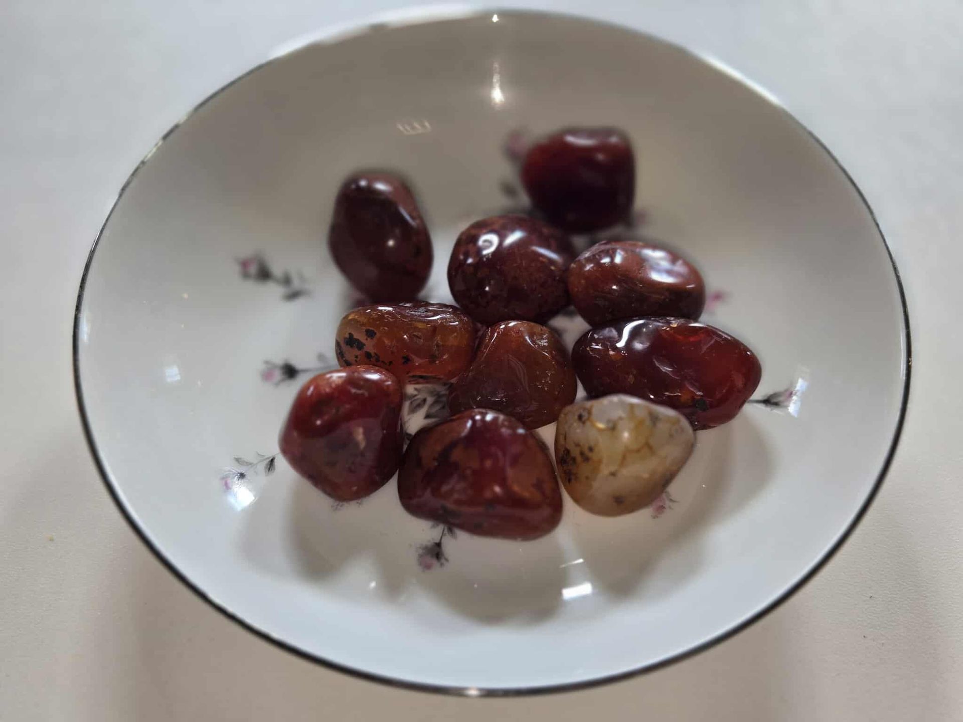Red-brown polished stones in a white floral dish on a white surface.