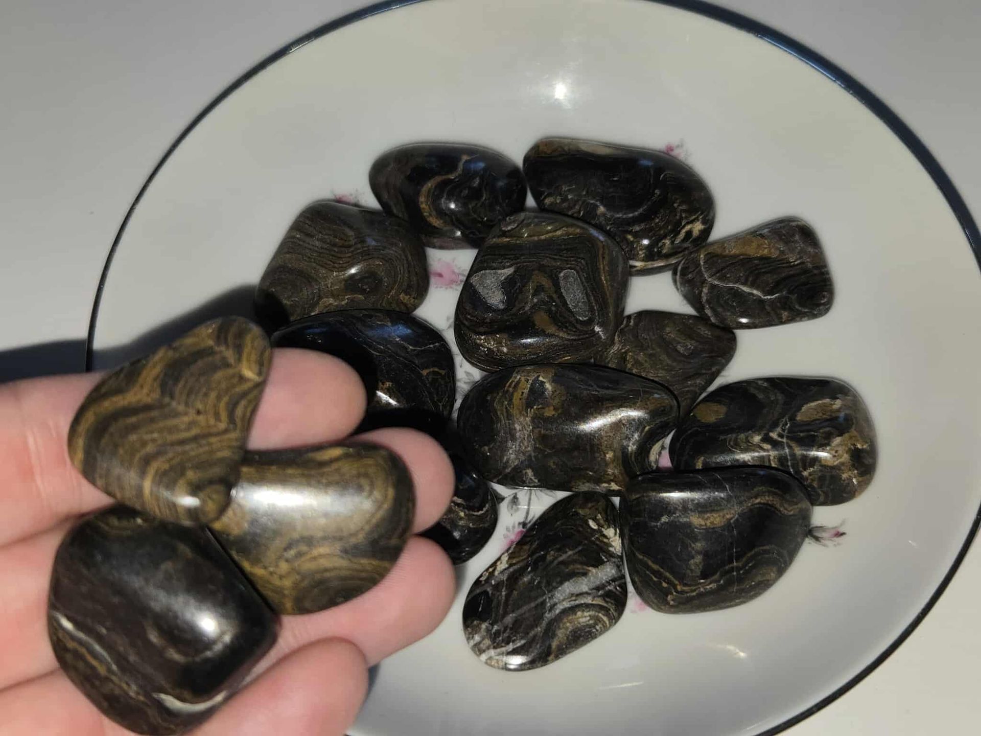 Black polished stones in a white bowl, sitting on a white surface.