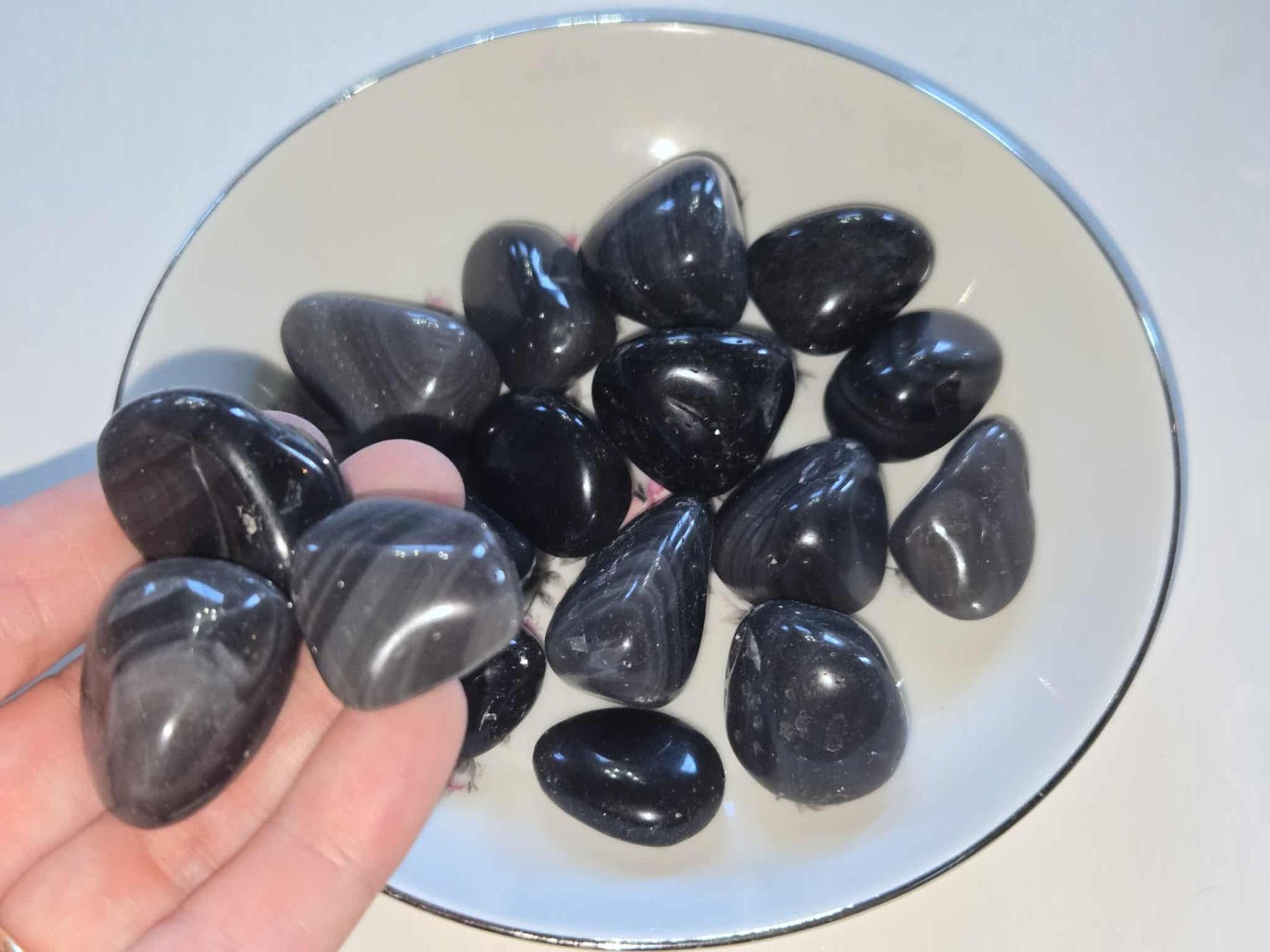 Black, polished stones in a white floral-decorated bowl, set on a white surface.