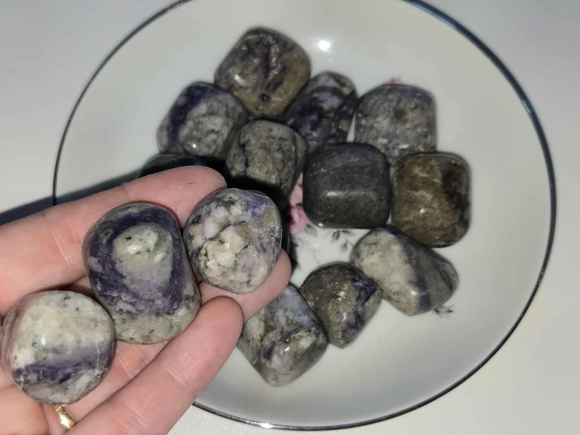 Tumbled gray and purple stones in a white dish with a floral pattern and a blue rim.