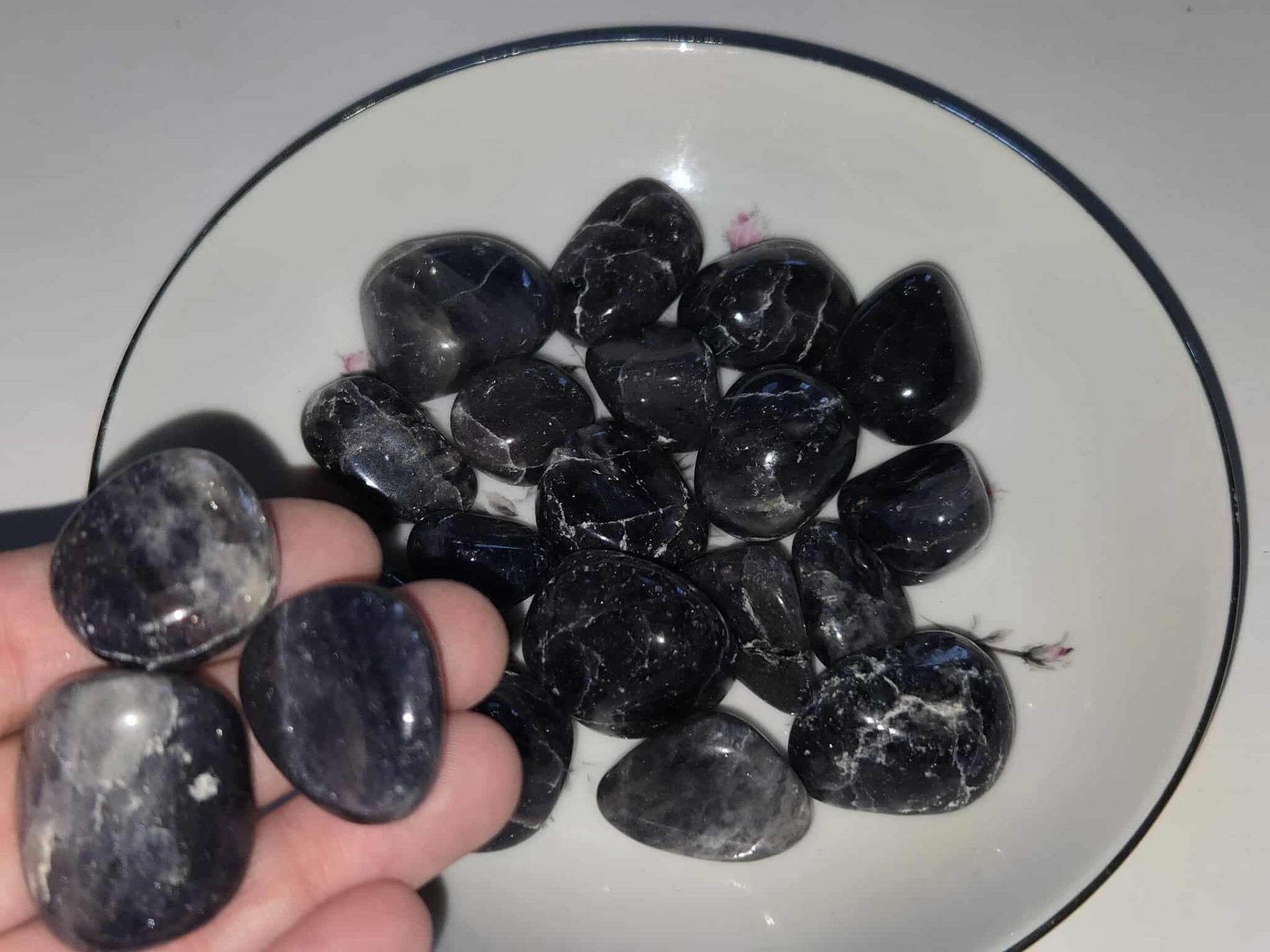 Black tumbled stones in a white floral-decorated bowl on a white surface.