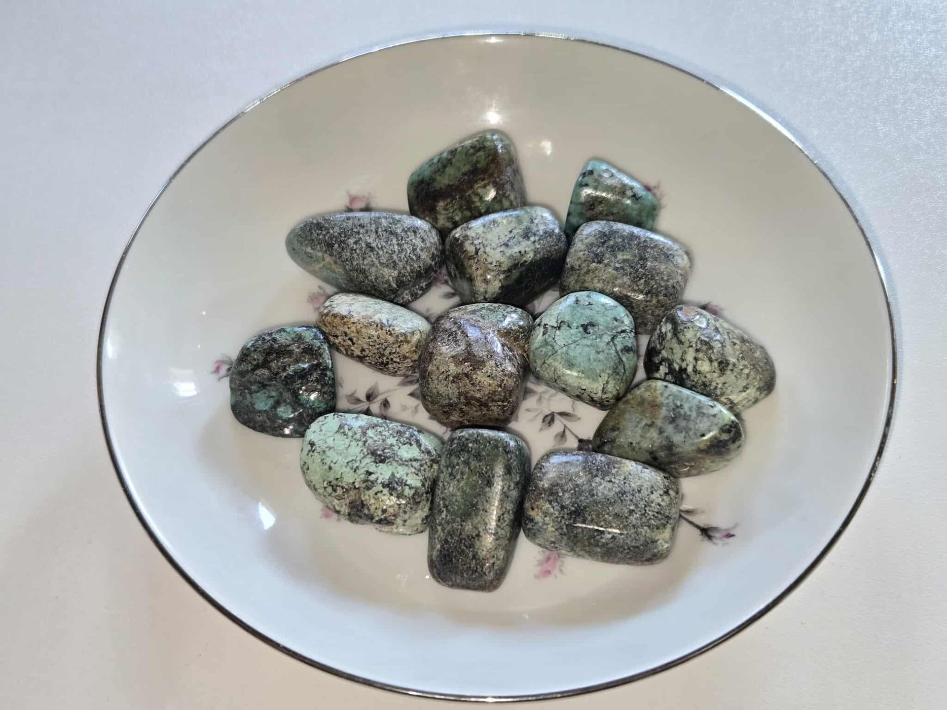 Tumbled turquoise-colored stones in a white floral-decorated dish with a silver rim.