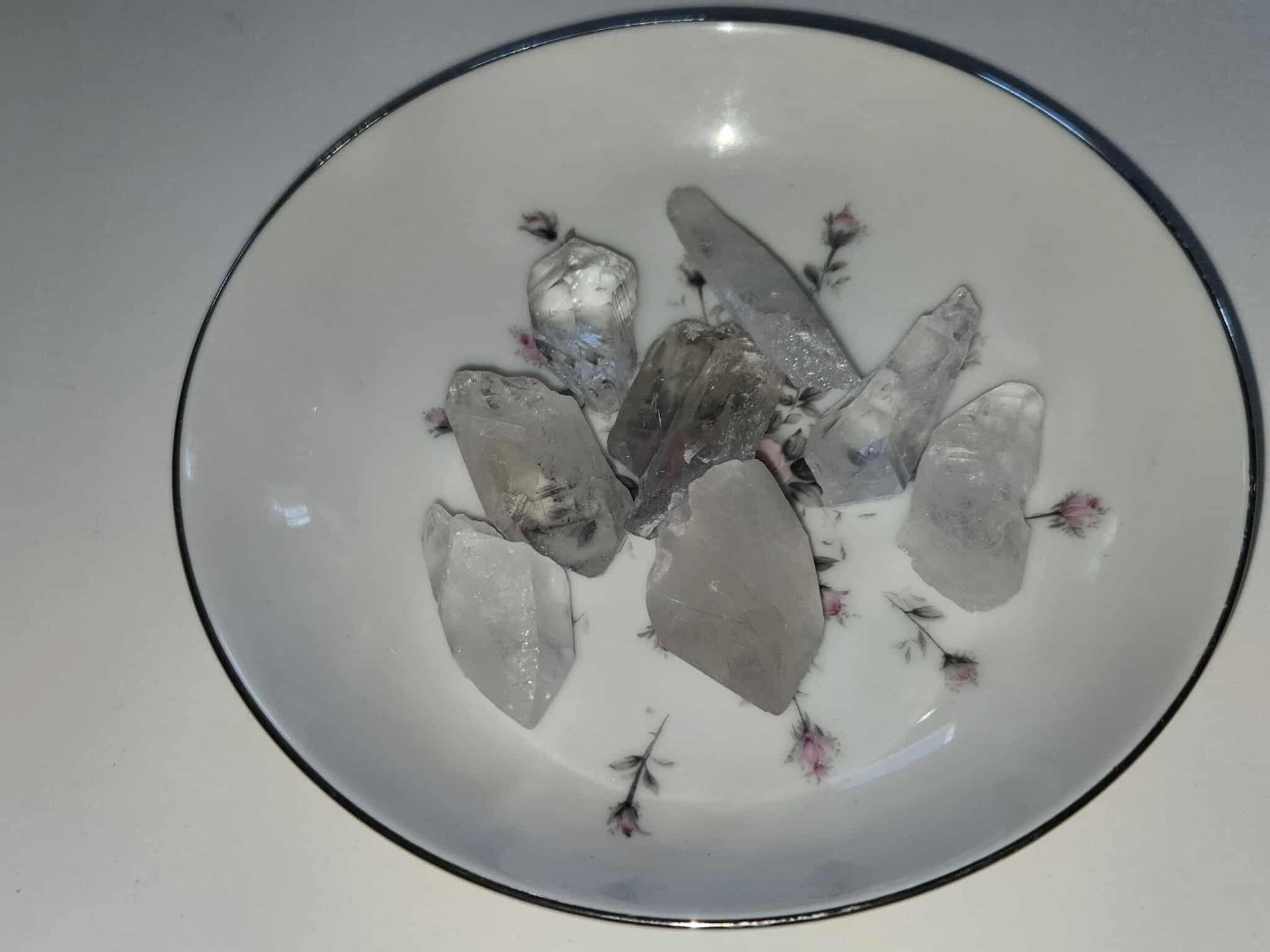 Clear quartz crystals arranged in a decorative white bowl with floral patterns.