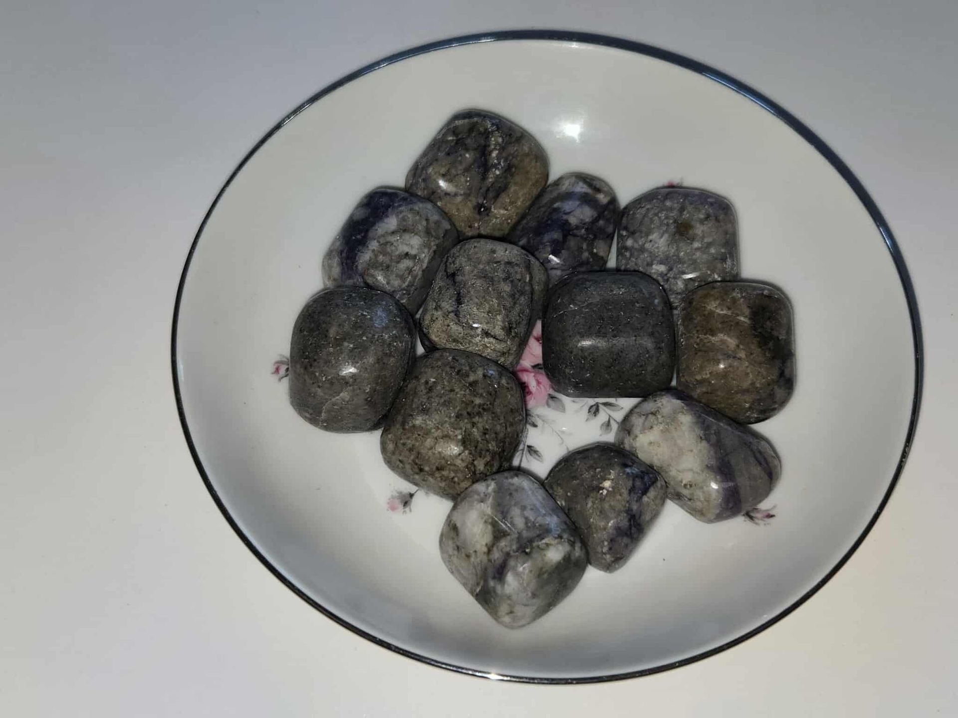 Tumbled gray and purple stones in a white dish with a floral pattern and a blue rim.