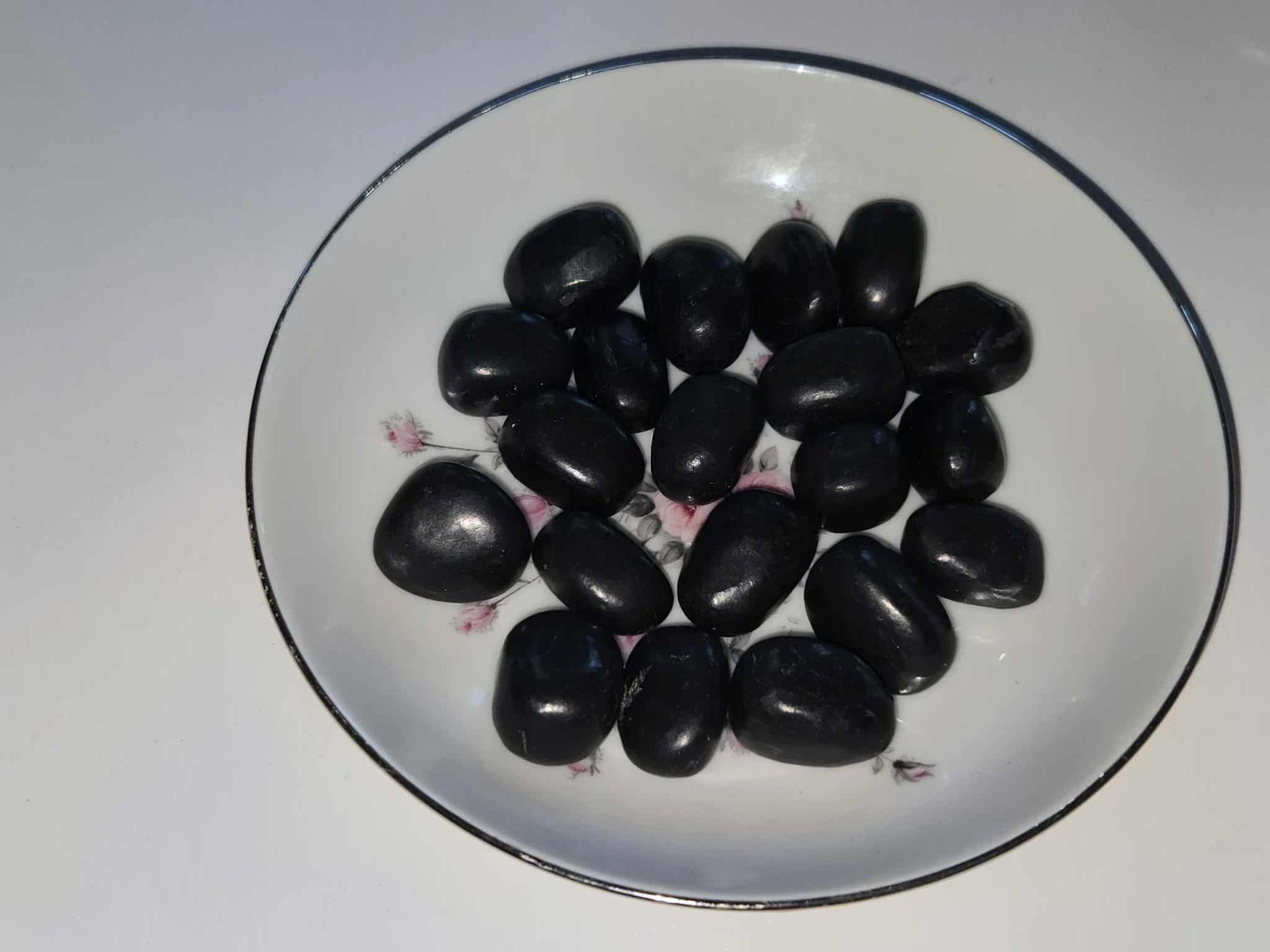 Black candies in a white and floral-patterned dish on a white surface.