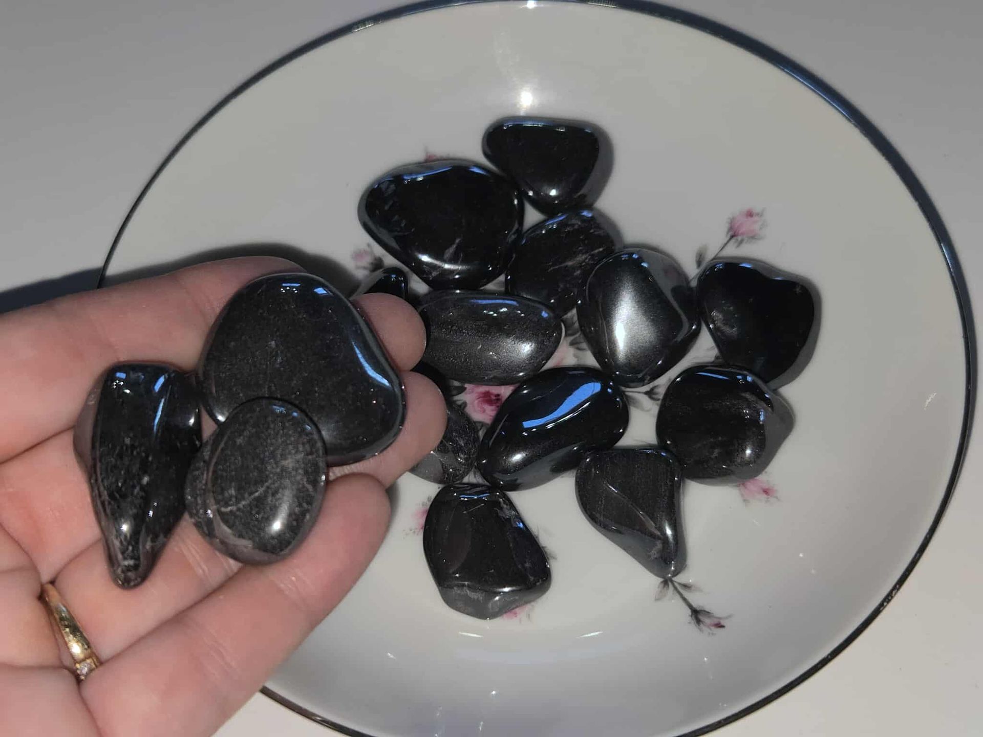 Black, polished stones in a white, floral-decorated bowl.
