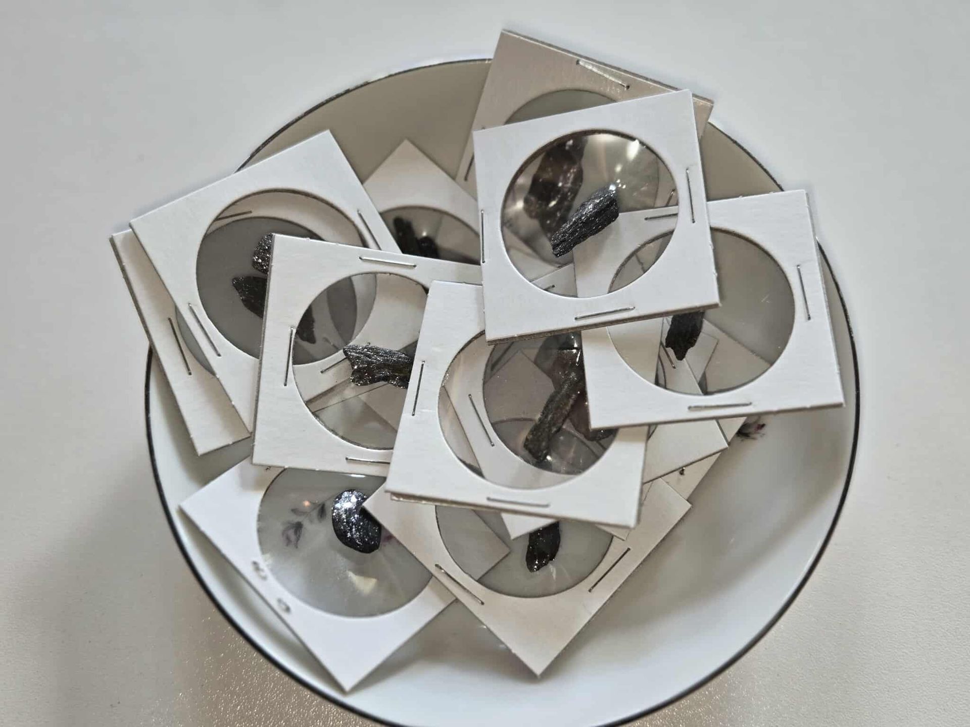 A white bowl filled with square white frames holding circular, reflective lenses.