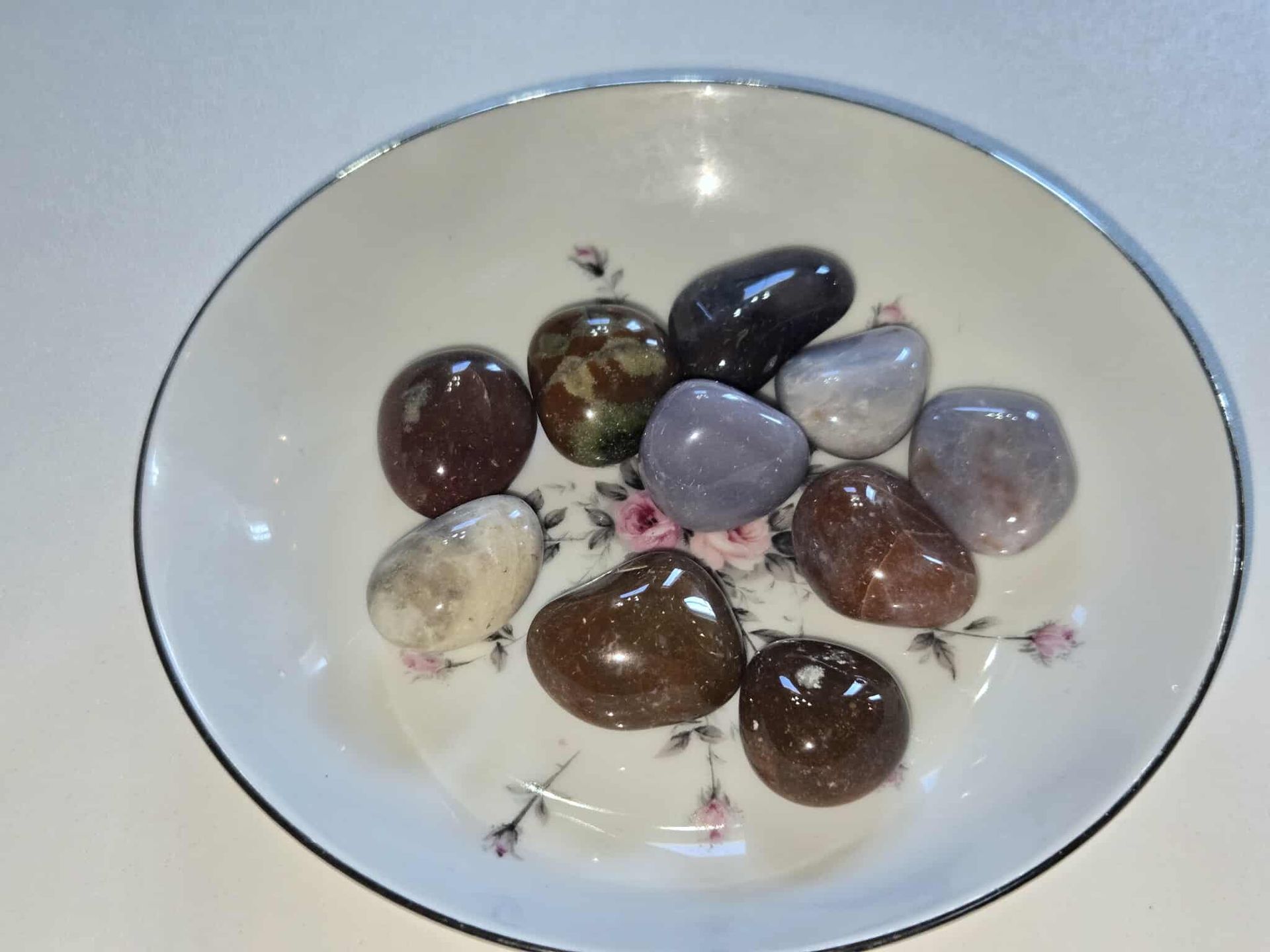 A white bowl with a floral design holds ten polished colorful stones.