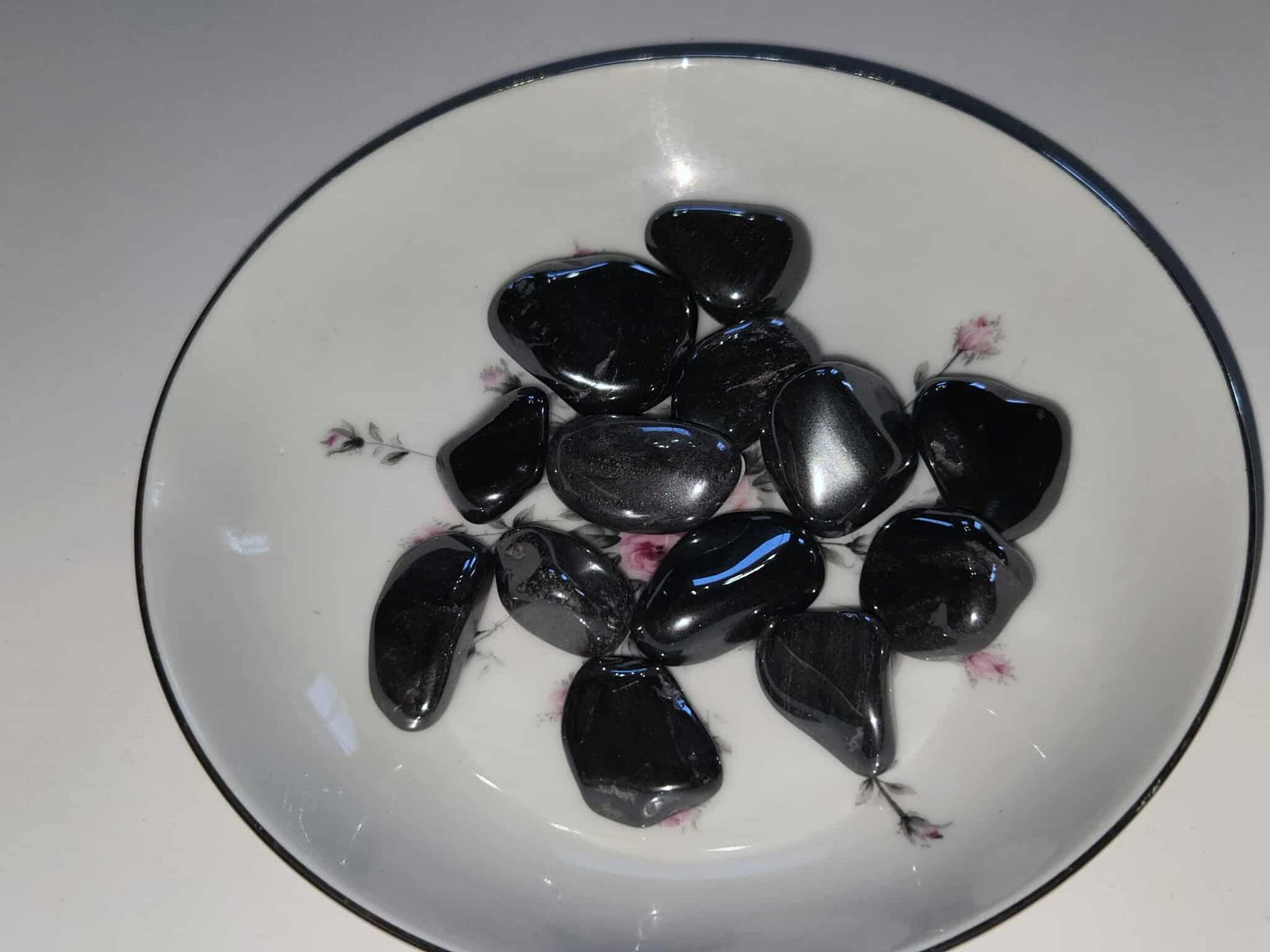 Black, polished stones in a white, floral-decorated bowl.