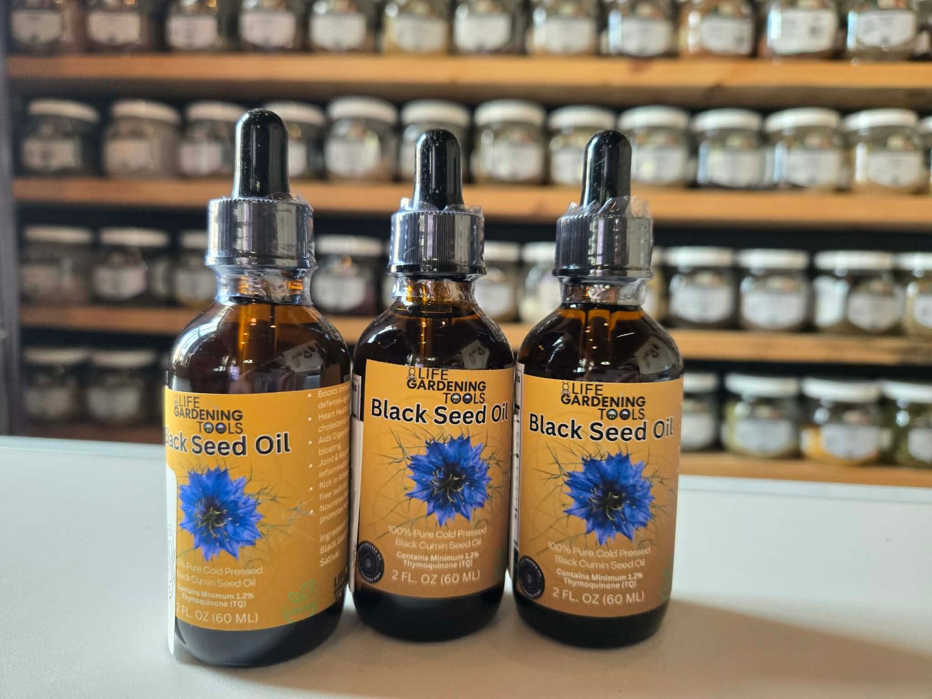 Three amber essential oil bottles with blue flowers on labels, displayed on a white counter in a shop.