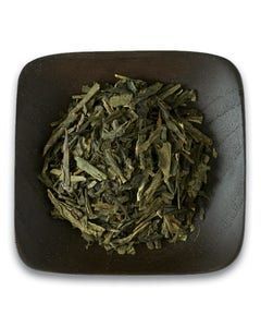 A wooden bowl filled with green tea leaves on a white background.