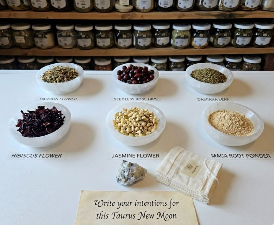 Jars and bowls of assorted ingredients on a table, labeled for a Taurus New Moon ritual.