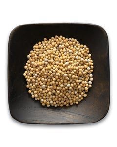 A wooden bowl filled with yellow mustard seeds on a white background.