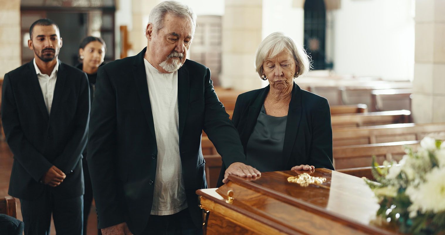 People grieving at a funeral: two touch the coffin, others stand behind them in a church.