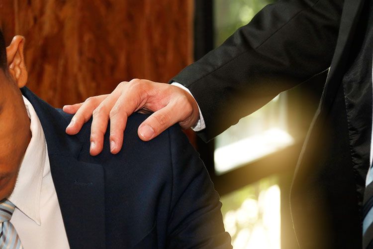 Man in suit comforts another by placing hand on their shoulder.