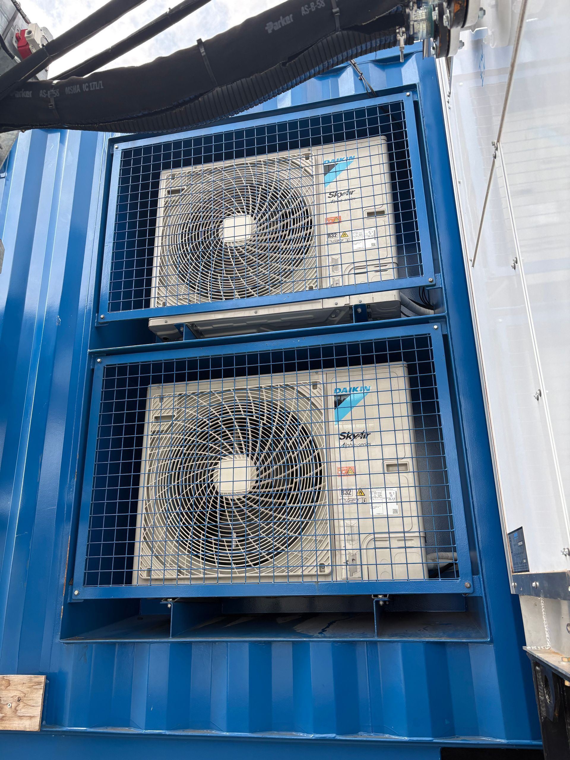 Two blue metal ventilation units with fans mounted on a corrugated wall