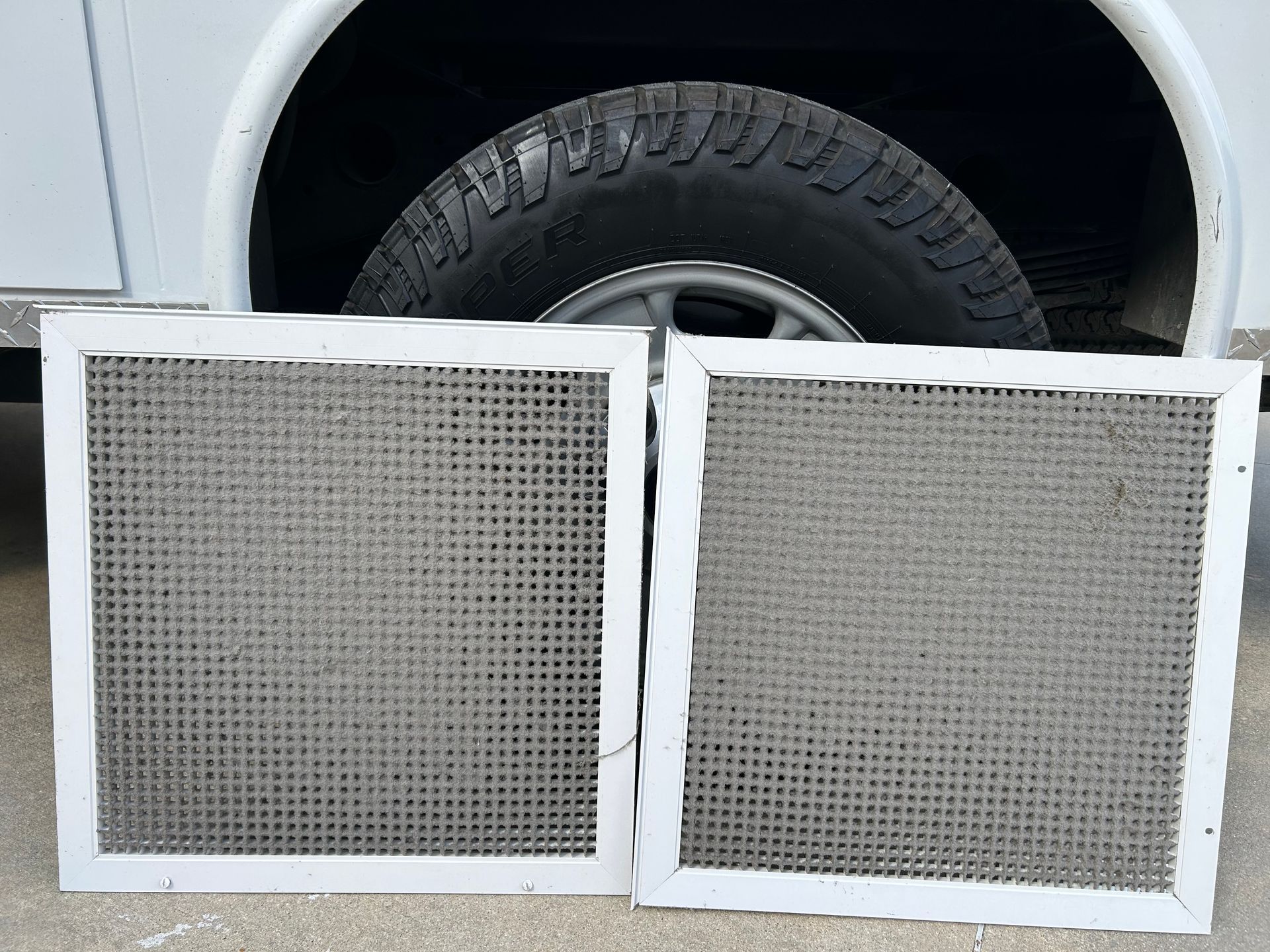 Two white-framed air filters leaning against a white vehicle tire on pavement