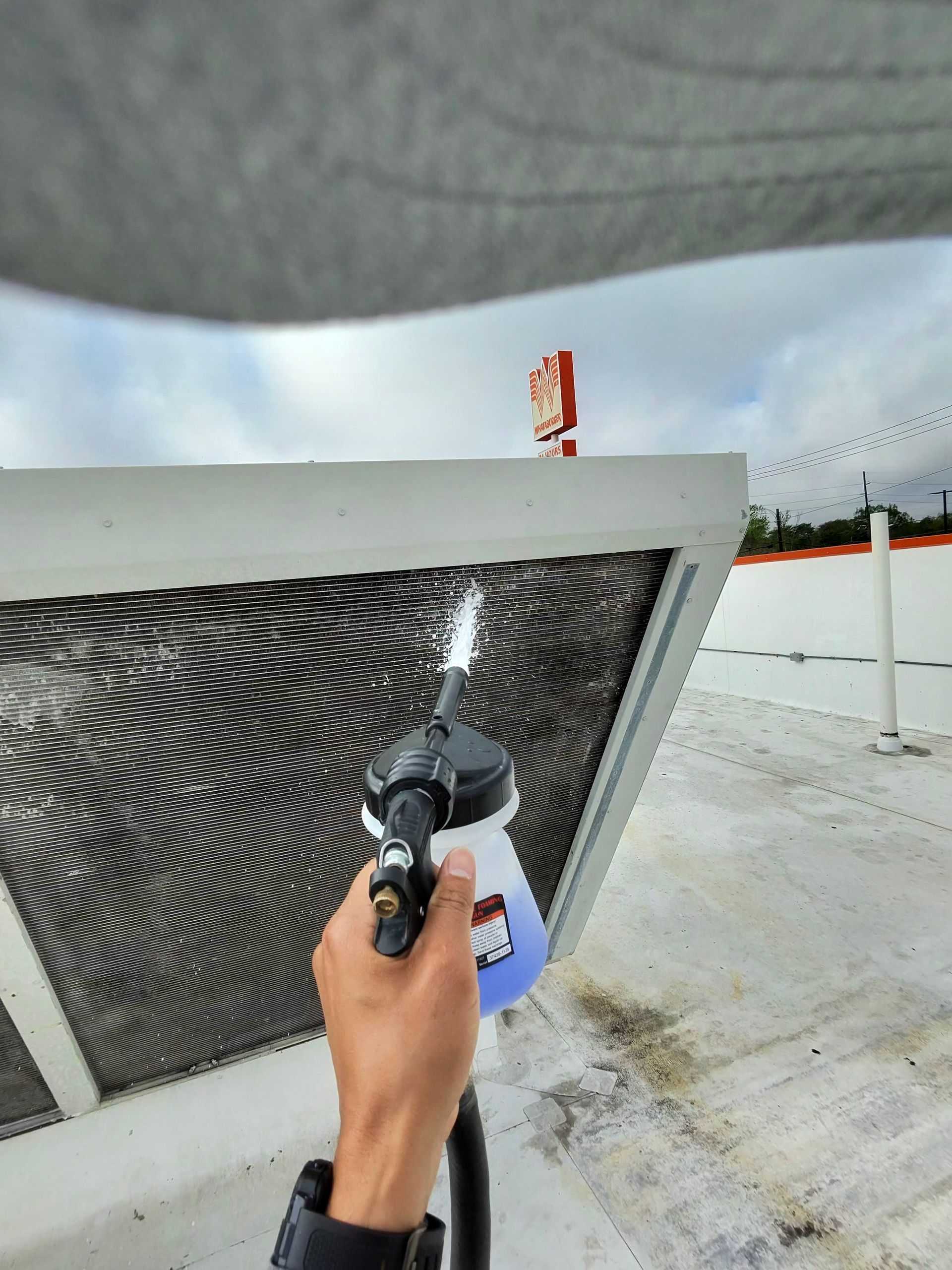 Hand holding a spray gun painting a large outdoor metal vent panel black and white