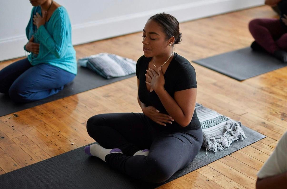 A group of people are sitting on a yoga mat with their hands in the air.