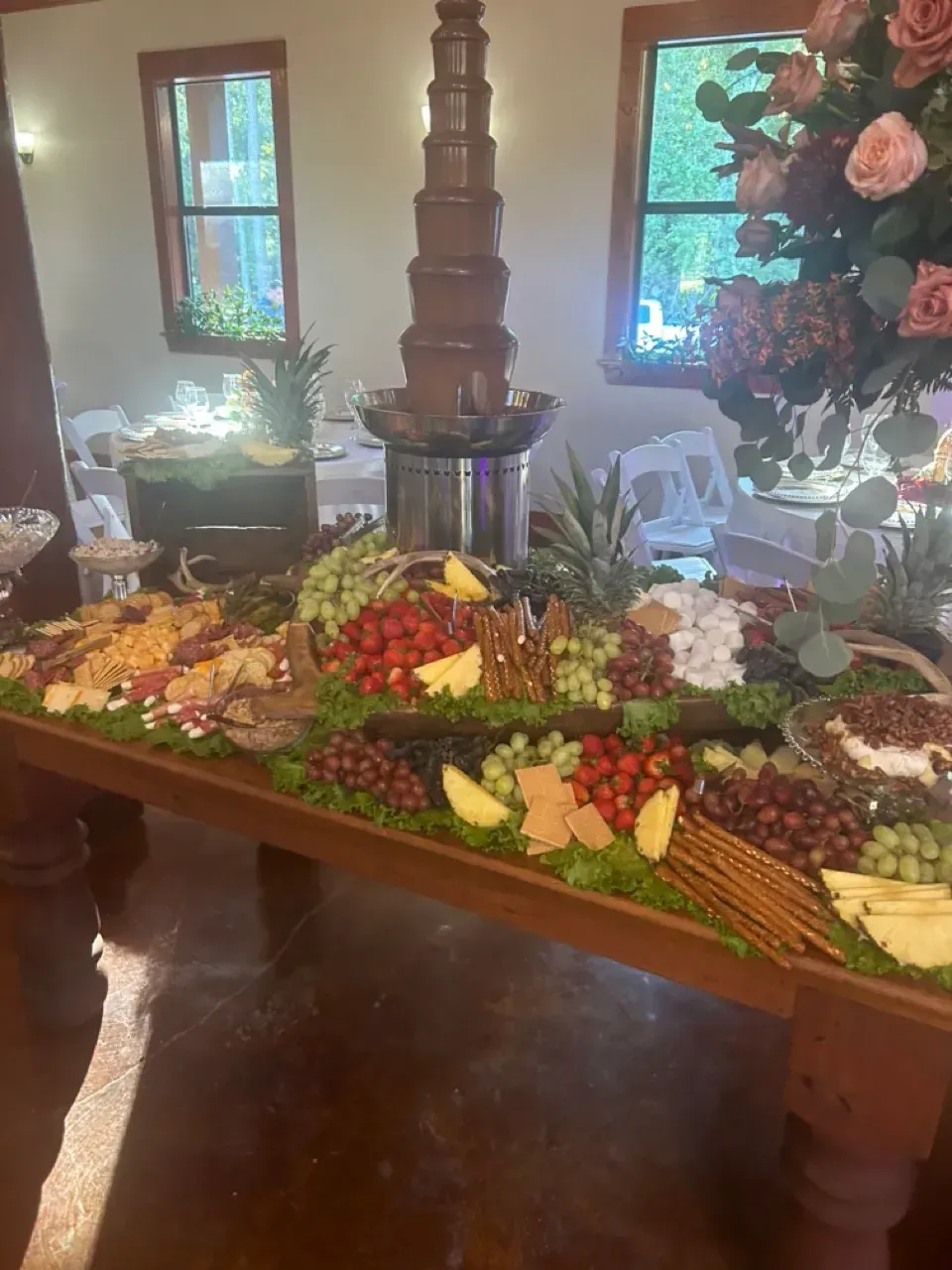 Large buffet table with fruit, cheese, and flowers in a warmly lit dining room