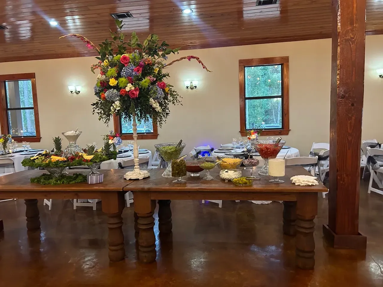 Long banquet table with food and a tall floral centerpiece in a rustic hall