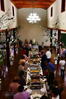 Long banquet table in a decorated hall with guests, floral arrangements, and a chandelier overhead