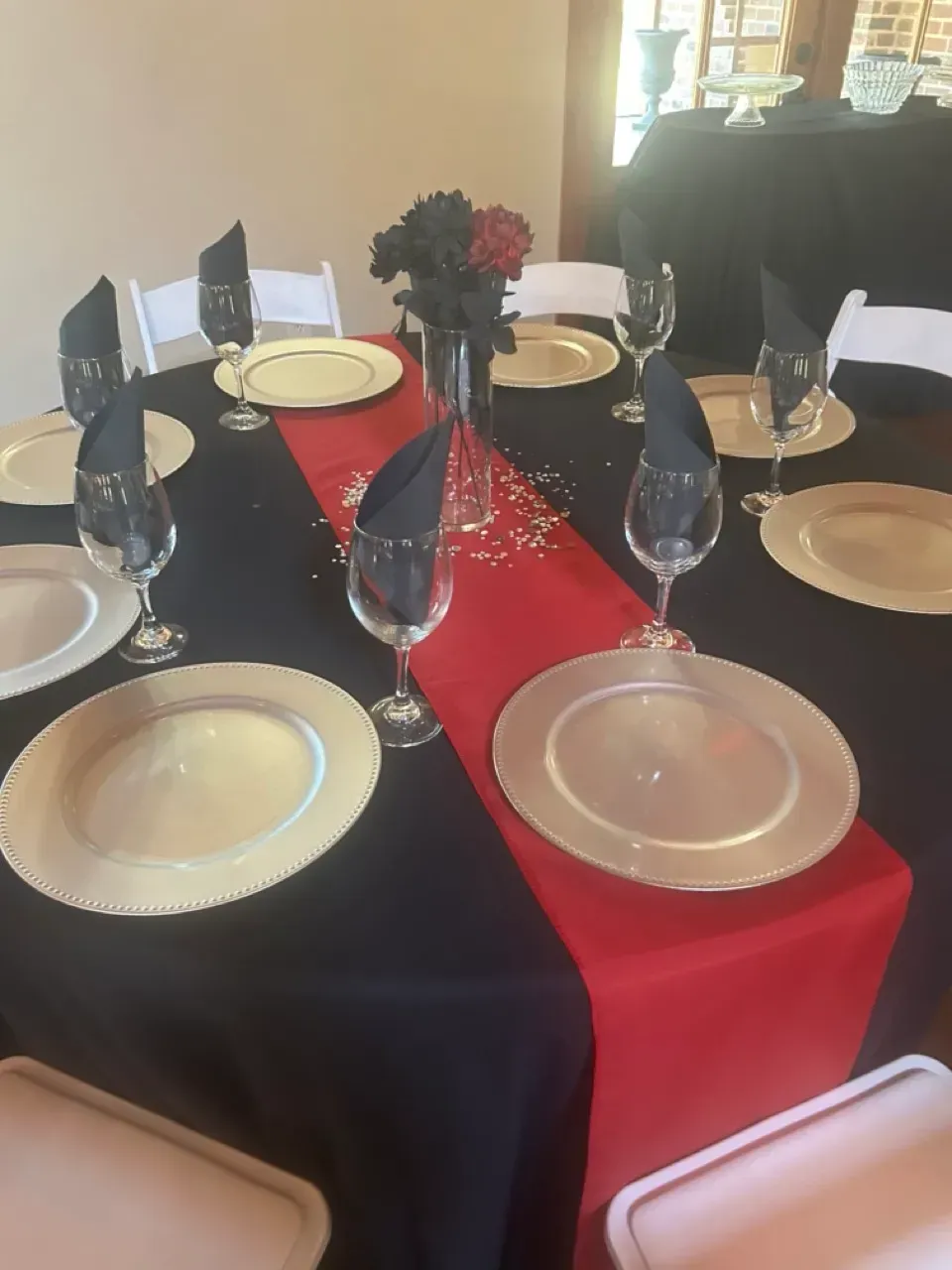 Formal dining table with black and red tablecloth, white plates, wine glasses, and flower centerpiece