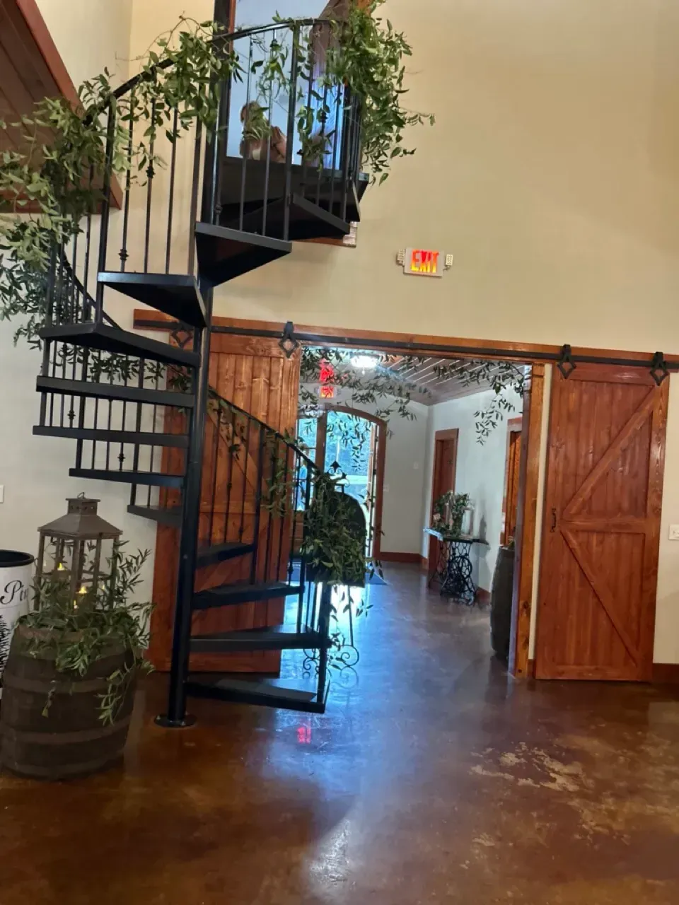 Spiral staircase in a rustic interior with wooden double doors and a potted plant by the entrance