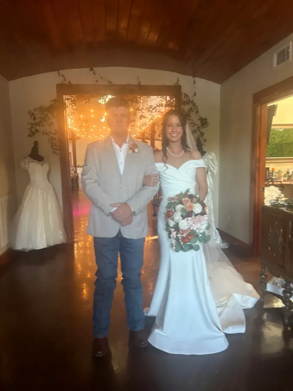 Bride and groom posing indoors at their wedding, bride holding bouquet in a white gown.