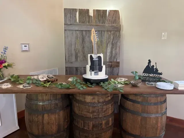 Rustic dessert table with cake on barrels, greenery, and small decor against a wooden backdrop
