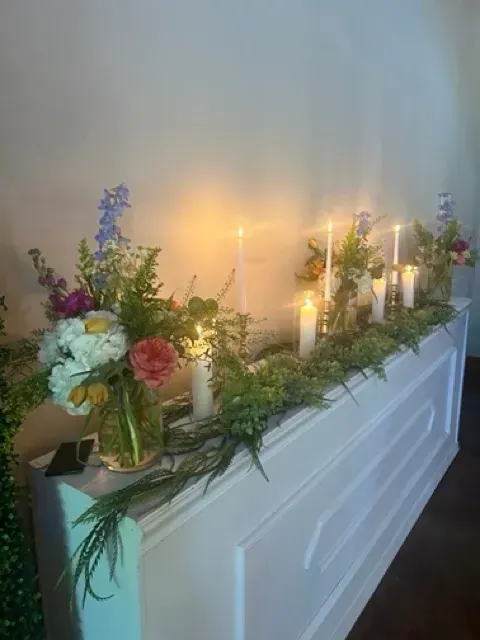 Floral arrangement with white, pink, and purple flowers and lit candles on a white mantelpiece