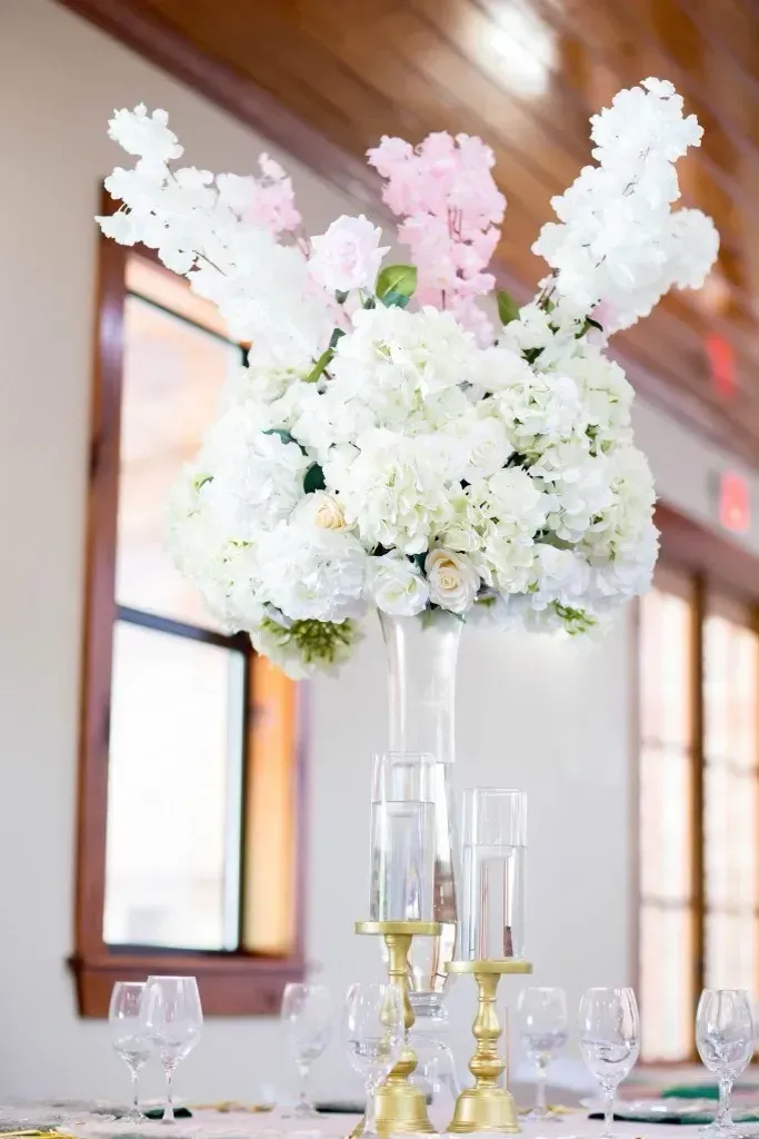 Tall white and blush floral arrangement in a glass vase on a decorated table in a bright room