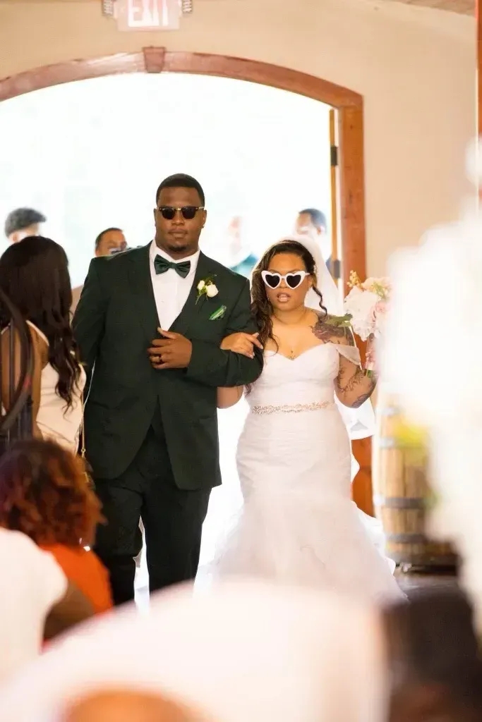 Bride and groom walking down the aisle, dressed in white and dark green, entering a bright ceremony space.