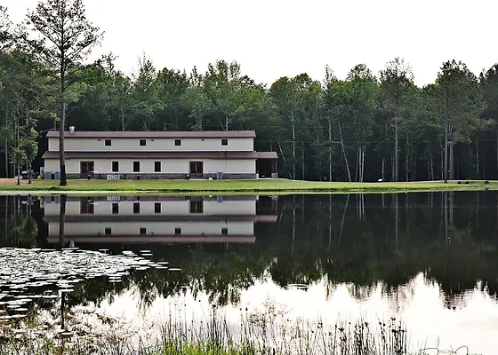 Lakeside building reflected in a calm pond, surrounded by trees.