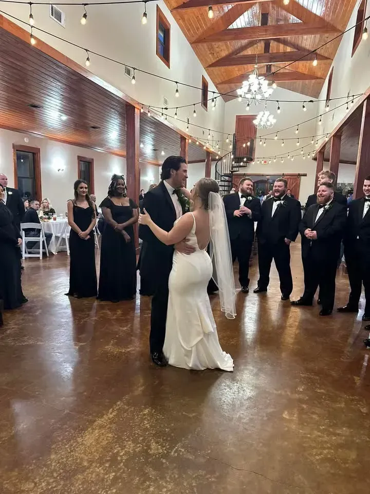 Bride and groom slow dancing in a rustic wedding hall with guests in formal attire watching